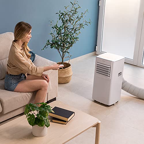 Femme utilisant climatiseur portable Cecotec dans salon moderne avec canapé beige et plante verte