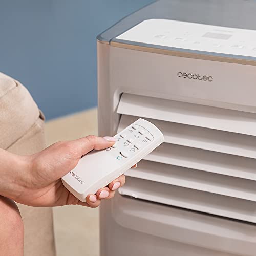 Main tenant télécommande blanche Cecotec devant grilles ventilation climatiseur, contrôle à distance
