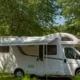 Camping-car blanc stationné à l ombre des arbres en plein été pour rester au frais en canicule