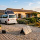 Camping-car équipé de panneaux solaires devant une maison avec un kit solaire à brancher posé au sol