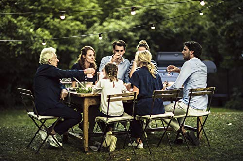 Groupe d'amis attablés au jardin le soir avec barbecue Campingaz en arrière-plan sous guirlande lumineuse