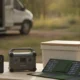 Matériel d énergie nomade (station portable, panneau solaire, glacière) et un smartphone affichant une courbe de prix, devant un camping-car